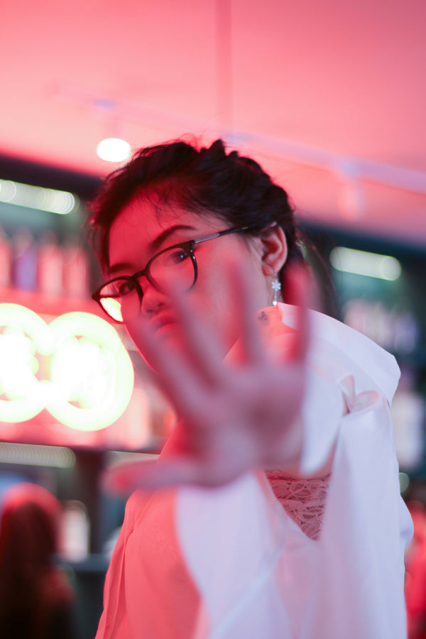 a woman holding her hand up with blue light glasses on her face